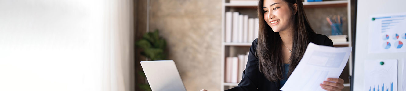 Woman at work holding a document and looking at her laptop.