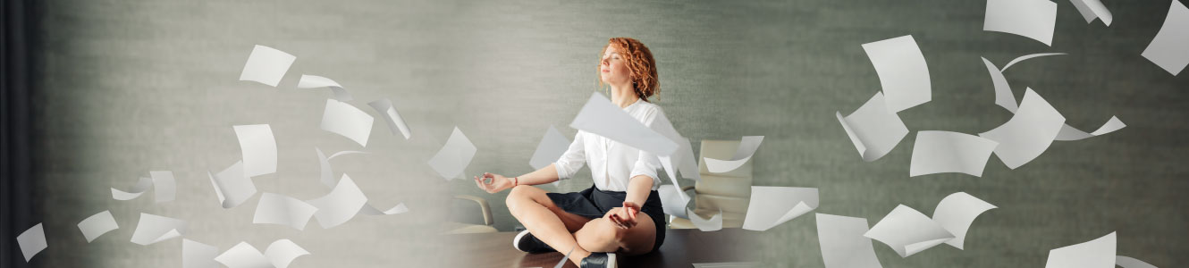 Women sitting on the ground meditating while papers are flying all around her