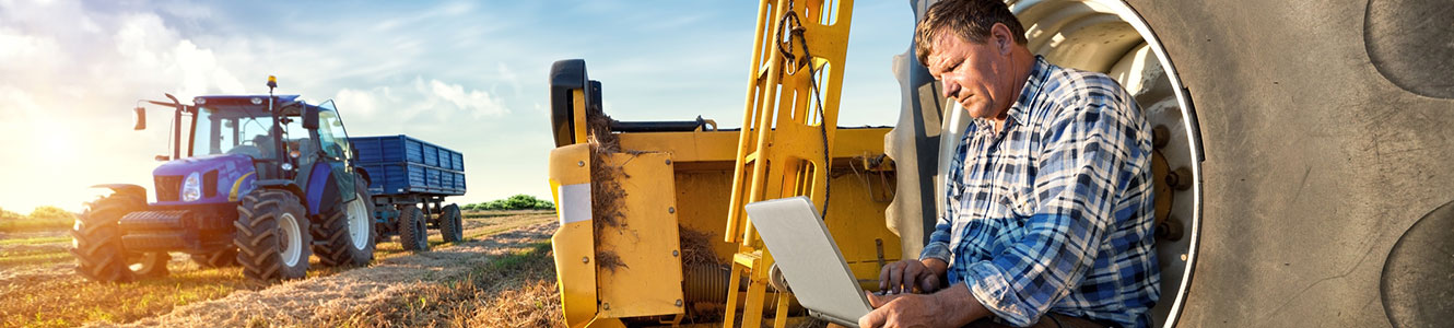 Farmer on laptop computer with farm equipment