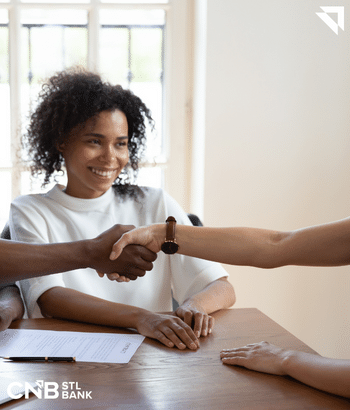 Two people shaking hands after a business deal while another woman is smiling that the deal was a success
